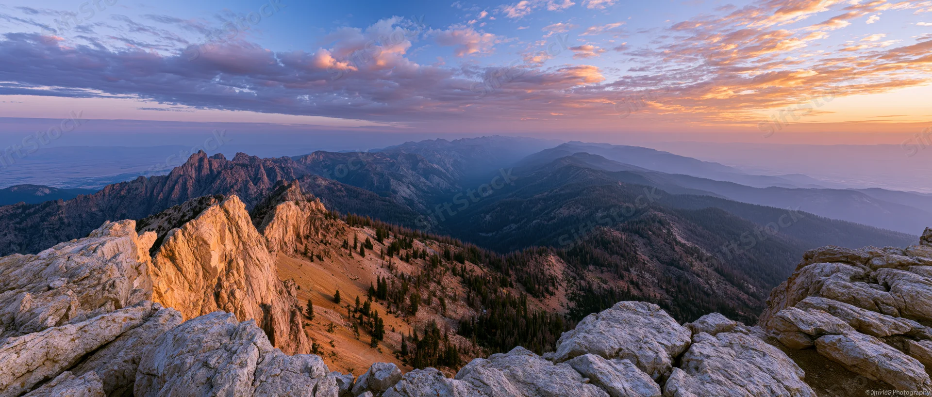 Alpine mountain panorama from rocky summit at sunset overlooking forested valleys and distant peaks