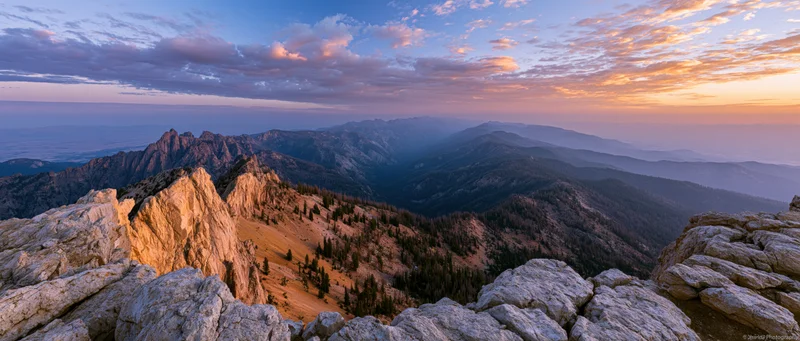 Alpine mountain panorama from rocky summit at sunset overlooking forested valleys and distant peaks