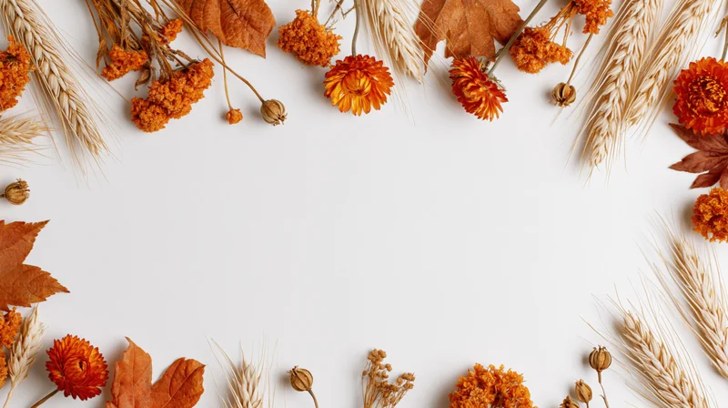 Dried orange flowers and wheat arranged in a border around white copyspace