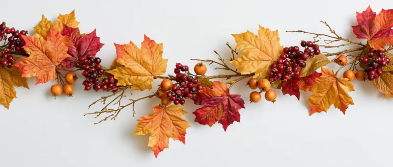 Autumn garland with maple leaves and berries arranged horizontally on white background