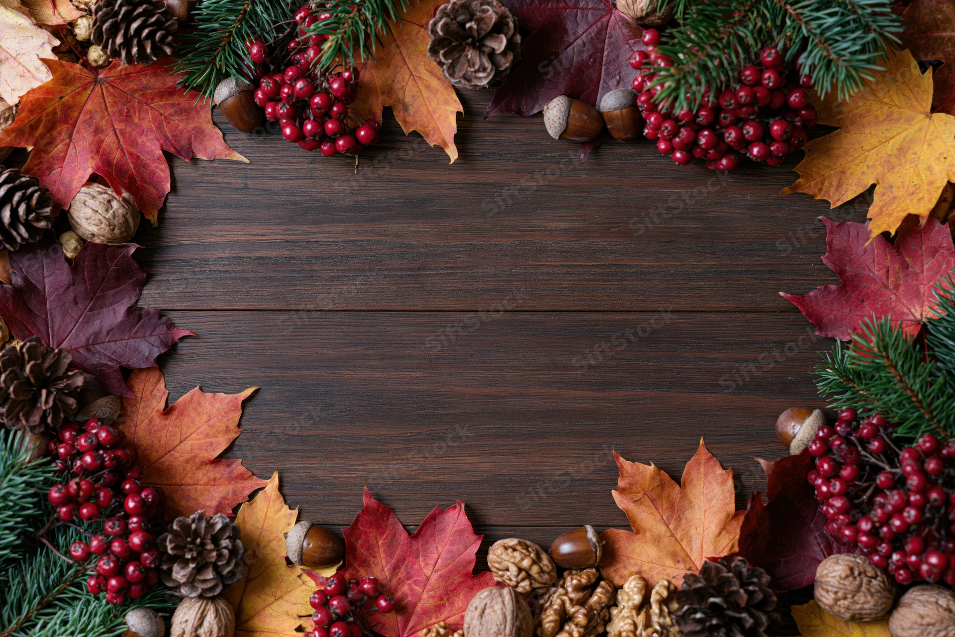 Autumn leaves and pinecones arranged in a border around a dark wooden table with copyspace in center