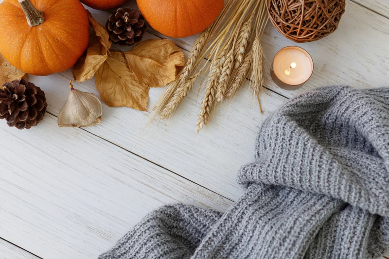 Autumn flat lay with pumpkins, wheat, pinecones, candle and gray sweater on white wooden table