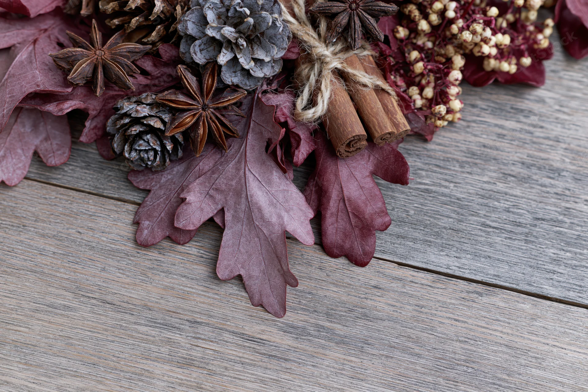 Dried burgundy oak leaves and pinecones arranged with cinnamon sticks and star anise on a rustic wooden table