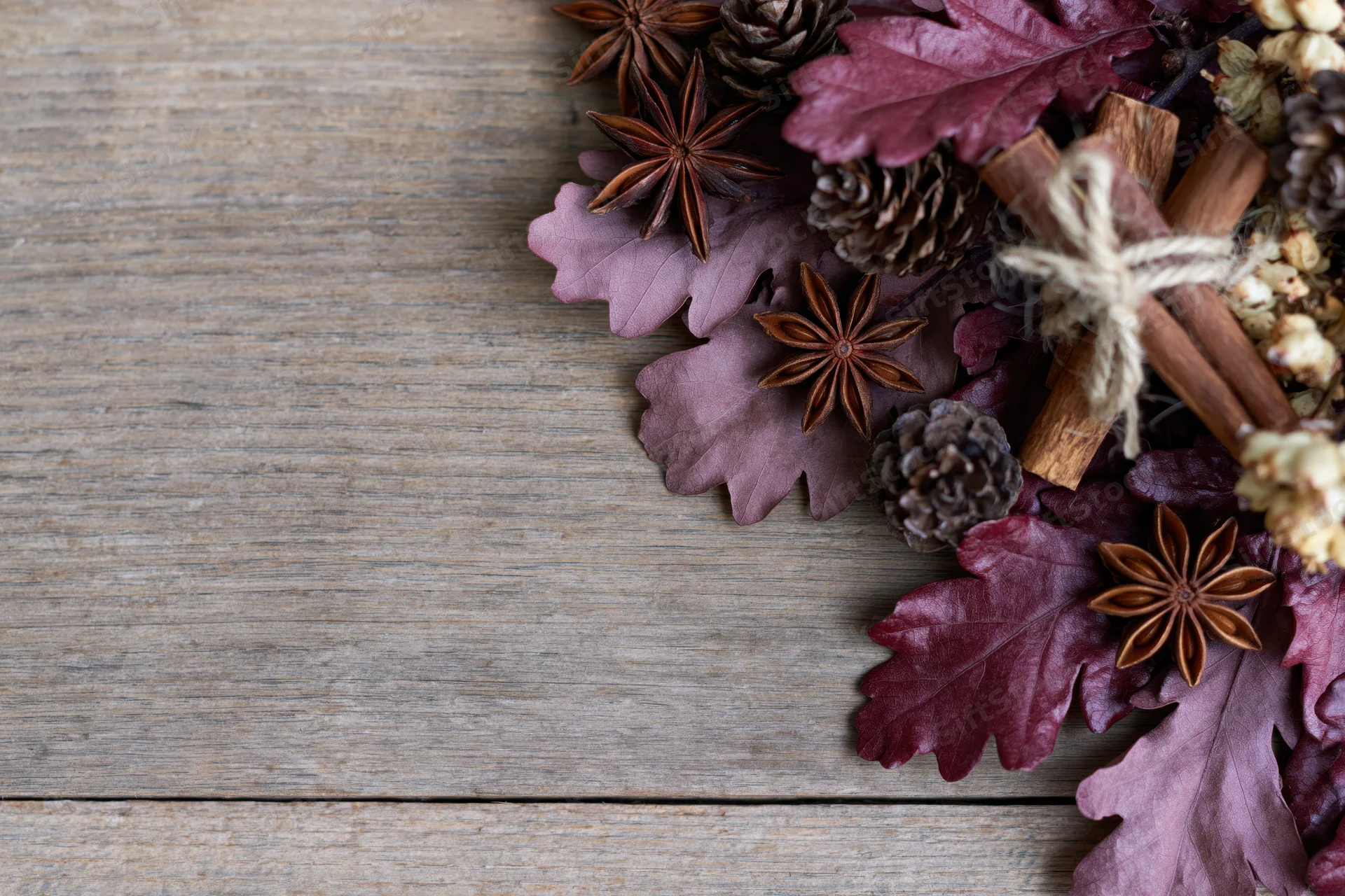 Autumn flat lay with dried burgundy oak leaves, pinecones, cinnamon sticks and star anise on rustic wooden table