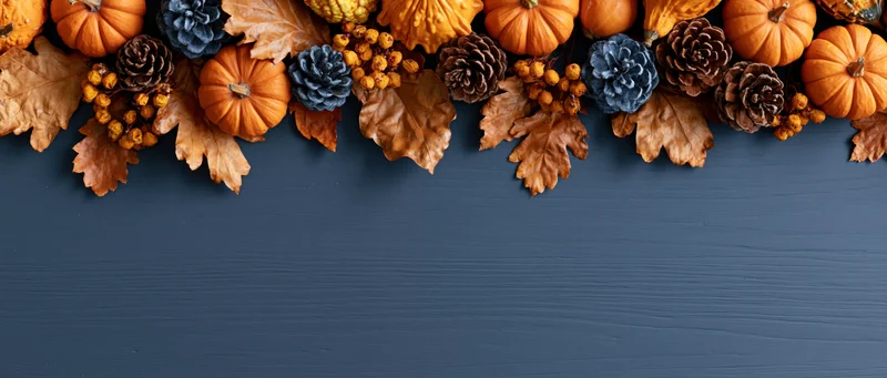 Autumn flat lay arrangement of pumpkins, leaves, pinecones and berries along dark blue wooden surface with copyspace below