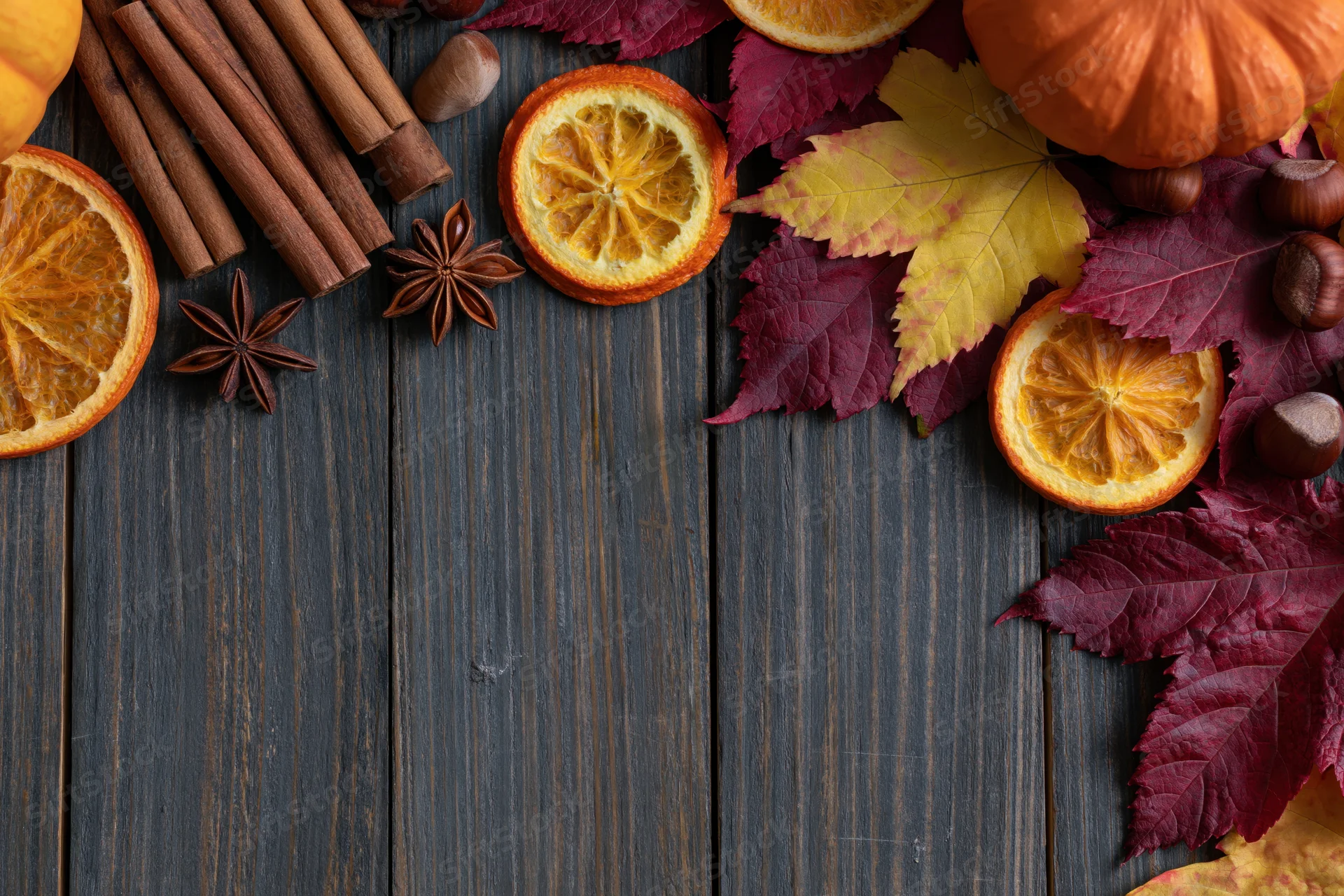 Autumn flat lay with dried orange slices, cinnamon sticks, pumpkins and leaves on dark wood table