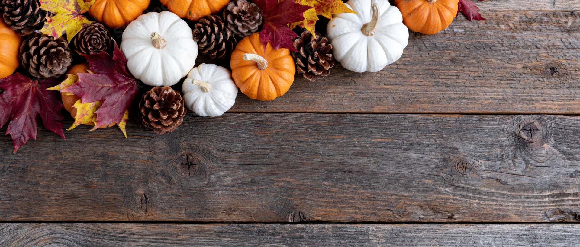 Autumn flat lay with small orange and white pumpkins, pinecones, and fall leaves arranged on a rustic wooden table