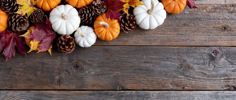 Autumn flat lay with small orange and white pumpkins, pinecones, and fall leaves arranged on a rustic wooden table
