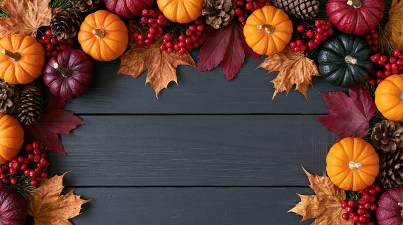 Autumn flat lay arrangement of small pumpkins, maple leaves, berries, and pinecones forming a border on dark wooden surface with central copyspace
