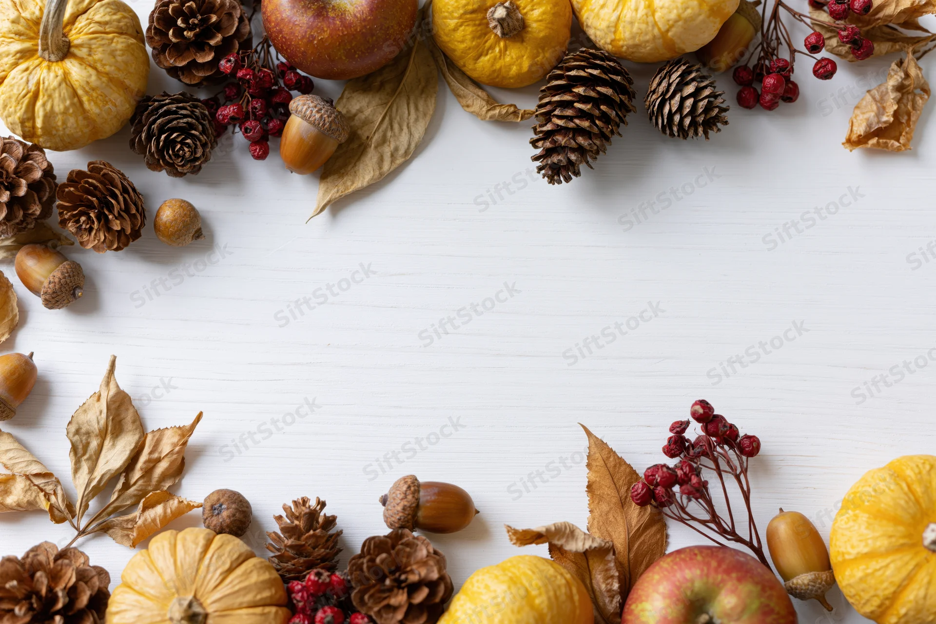 Autumn flat lay arrangement of pumpkins, pinecones, apples, and dried leaves on white wooden surface forming border with copyspace