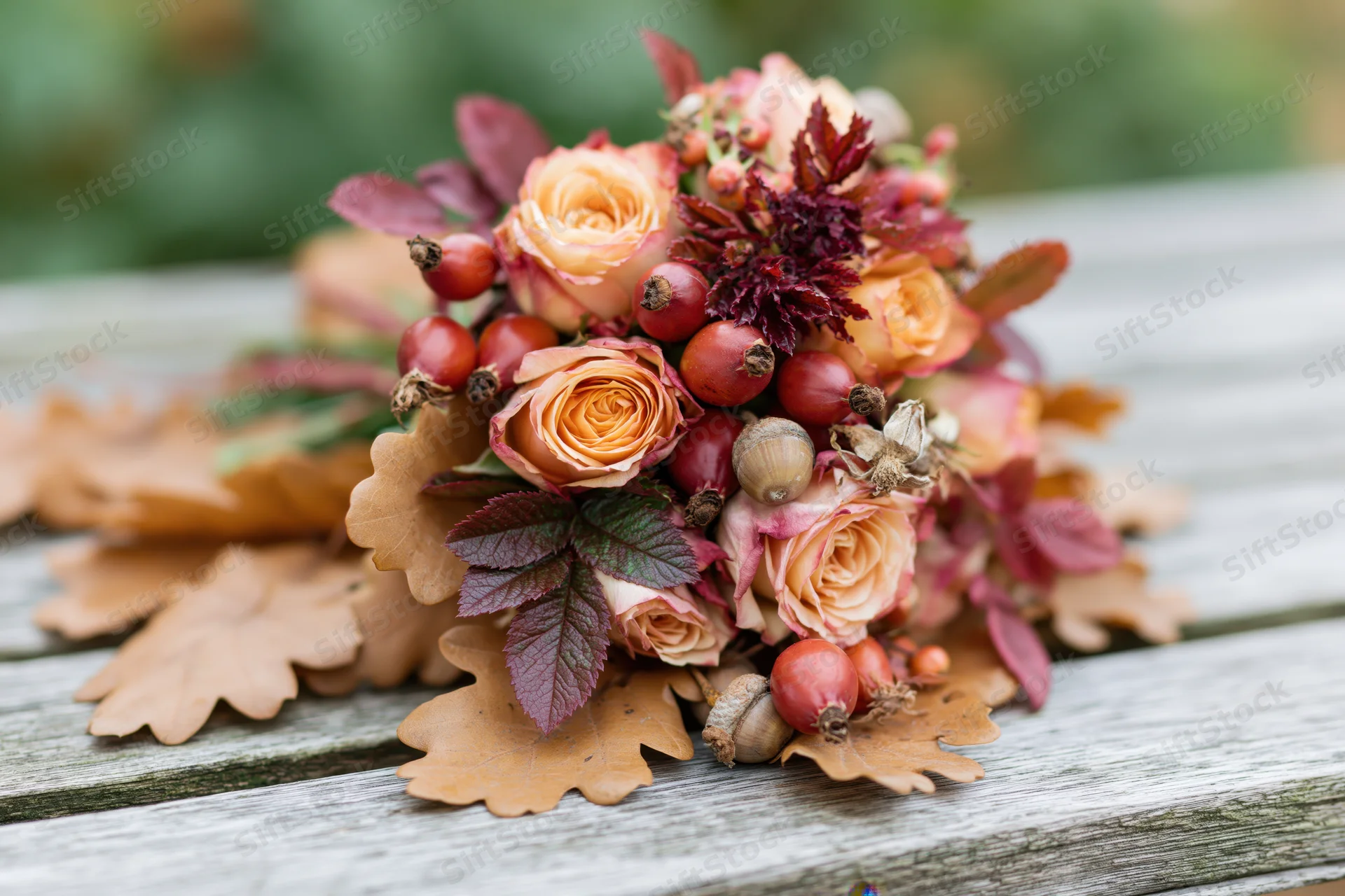 Autumn floral bouquet with roses, rosehips, acorns and oak leaves resting on a weathered wooden bench