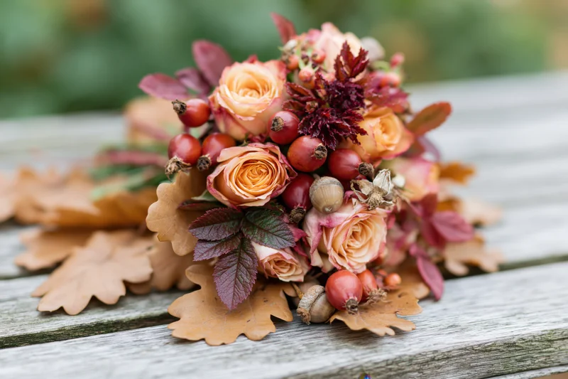 Autumn floral bouquet with roses, rosehips, acorns and oak leaves resting on a weathered wooden bench