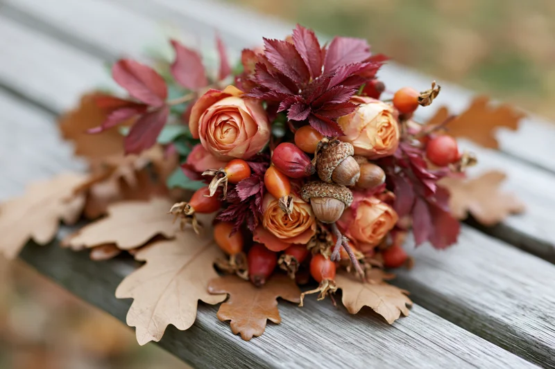 Autumn floral arrangement with roses, acorns and berries on a weathered wooden bench