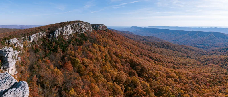 Autumn forest covering steep mountain slopes with rocky limestone cliffs under a clear blue sky