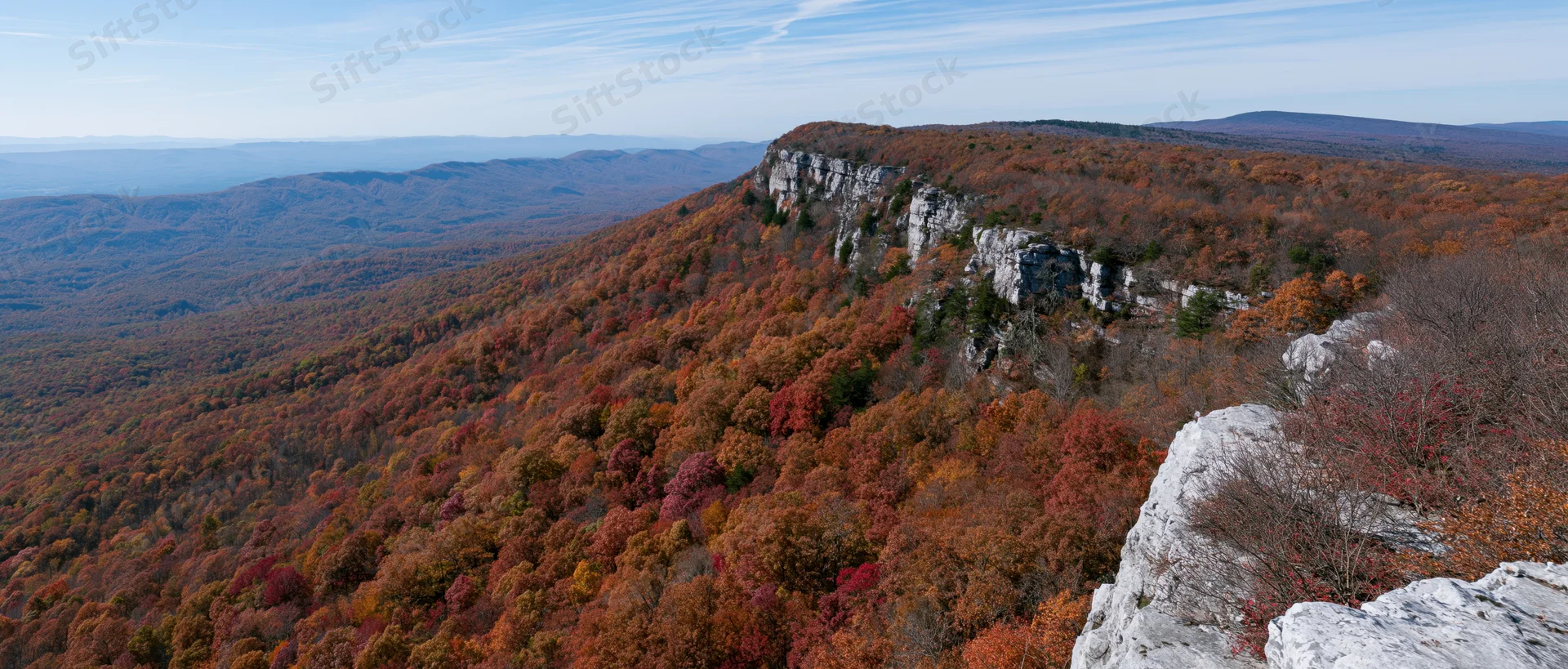 Autumn forest covering steep mountain slopes with rocky limestone cliffs under a clear sky
