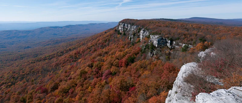 Autumn forest covering steep mountain slopes with rocky limestone cliffs under a clear sky