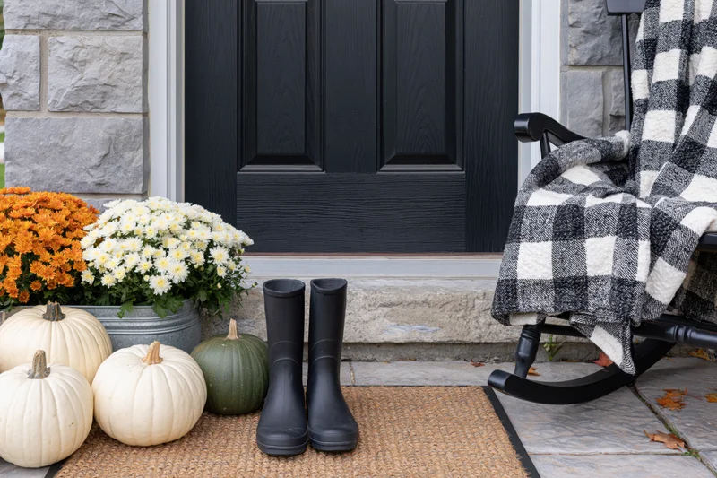 Autumn-decorated front porch with white and green pumpkins, flowers, and rocking chair draped in checkered blanket