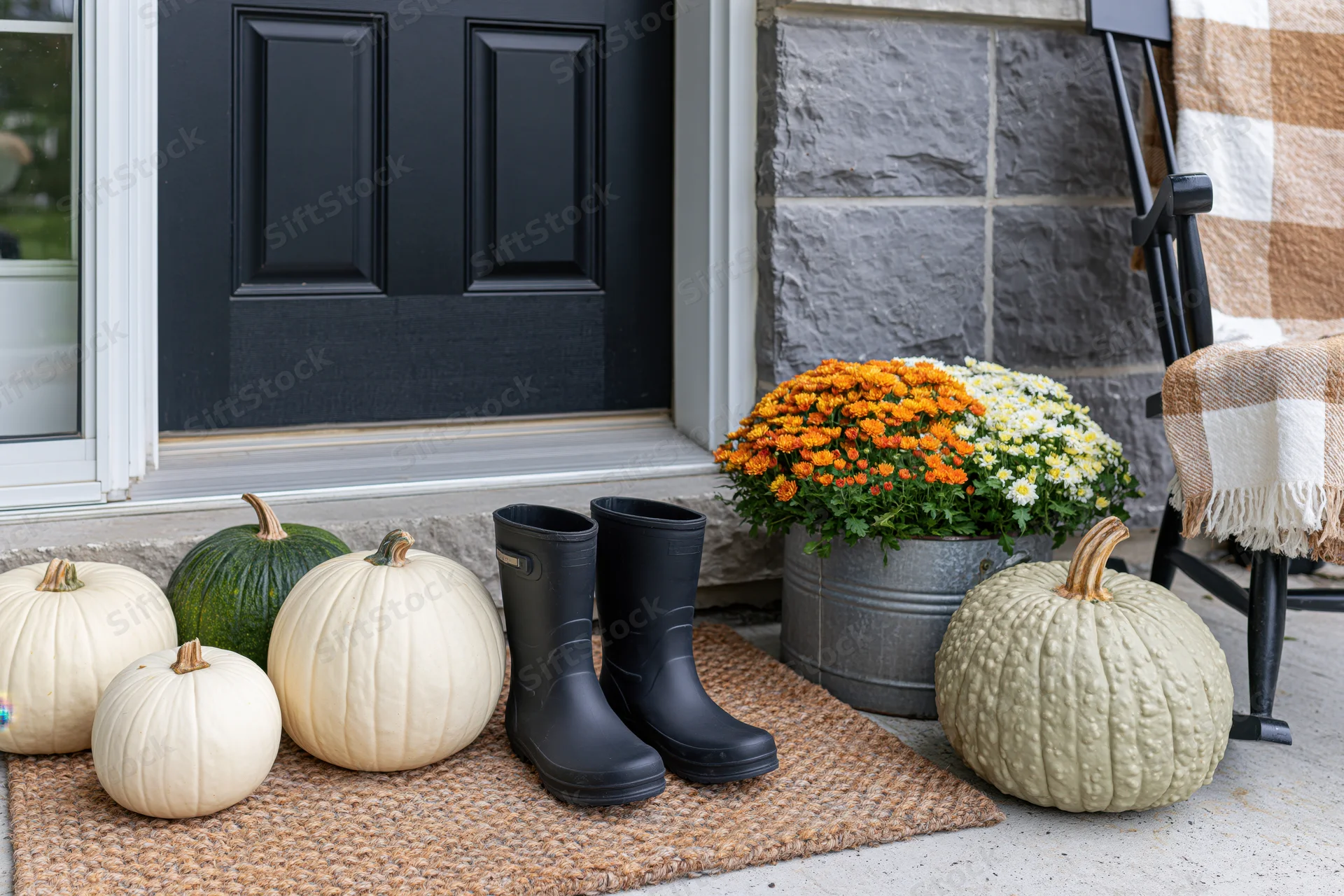 Autumn front porch decorated with white and green pumpkins, black boots, and orange and white mums in a metal bucket near a black door