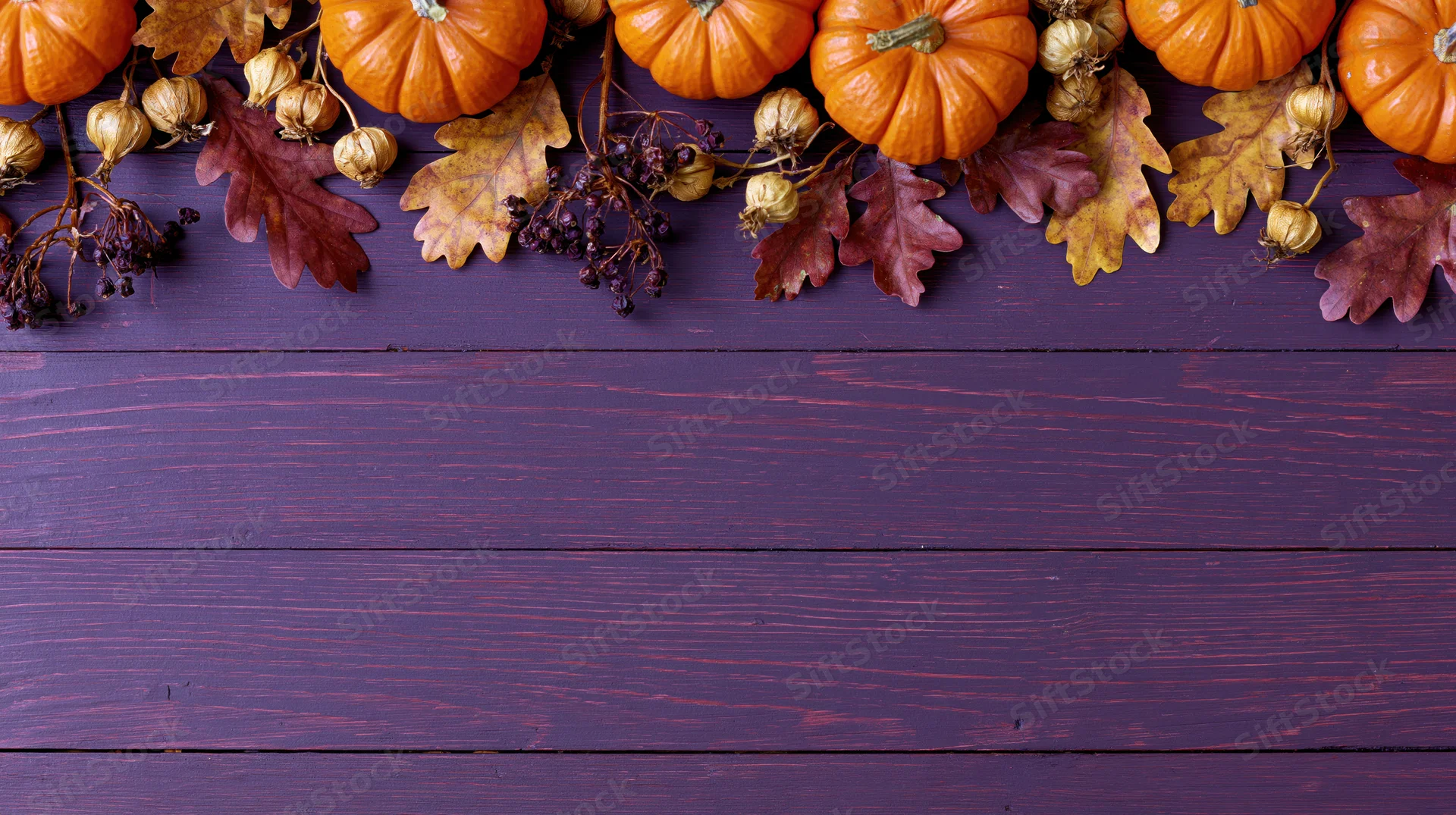 Autumn harvest flat lay with pumpkins and leaves arranged along the top edge of a purple wooden table