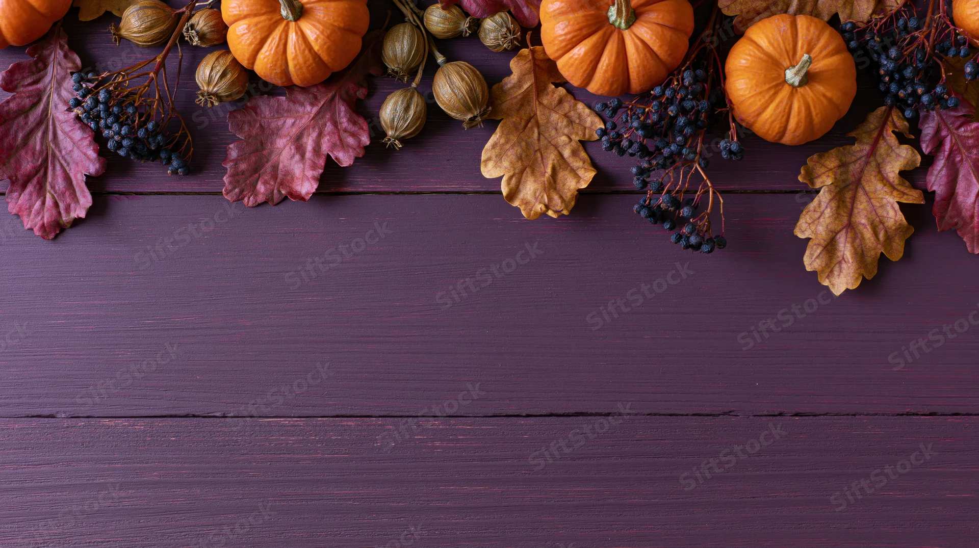 Autumn harvest flat lay with pumpkins, leaves and berries arranged along the top edge of a purple wooden table