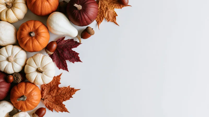 Small pumpkins and autumn leaves arranged in a corner flat lay on white surface