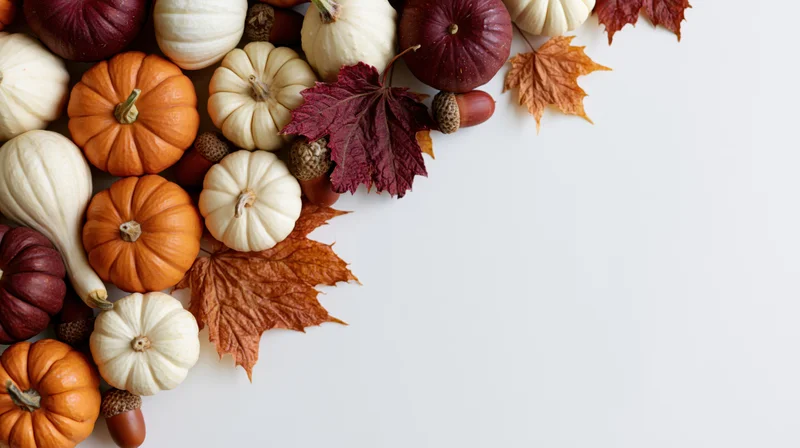 Small pumpkins and autumn leaves arranged in a flat lay on white surface with copyspace