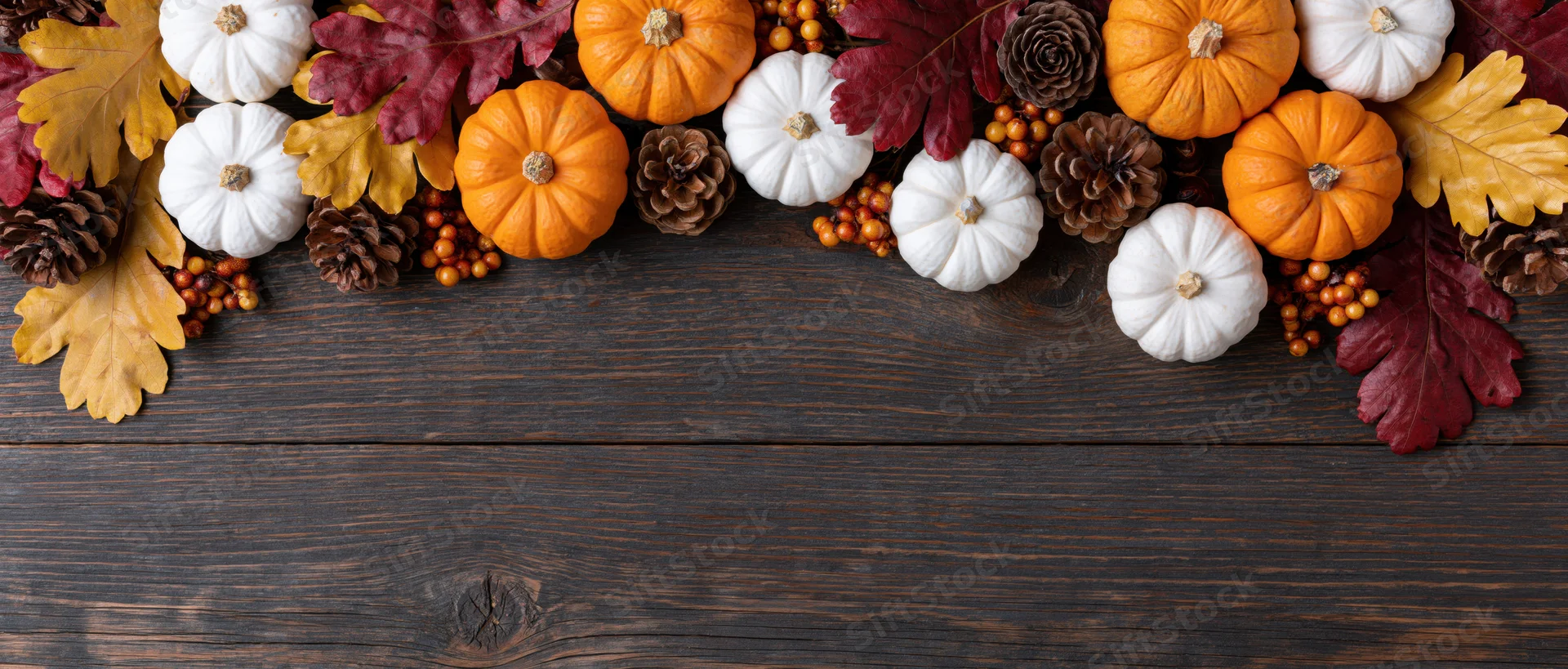 Small orange and white pumpkins arranged with autumn leaves and pinecones on dark wooden table
