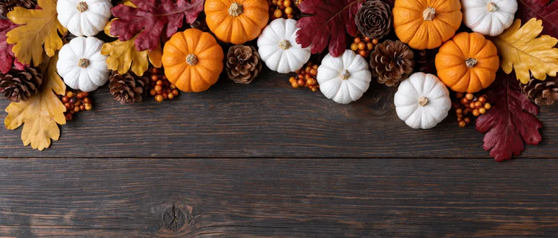 Small orange and white pumpkins arranged with autumn leaves and pinecones on dark wooden table