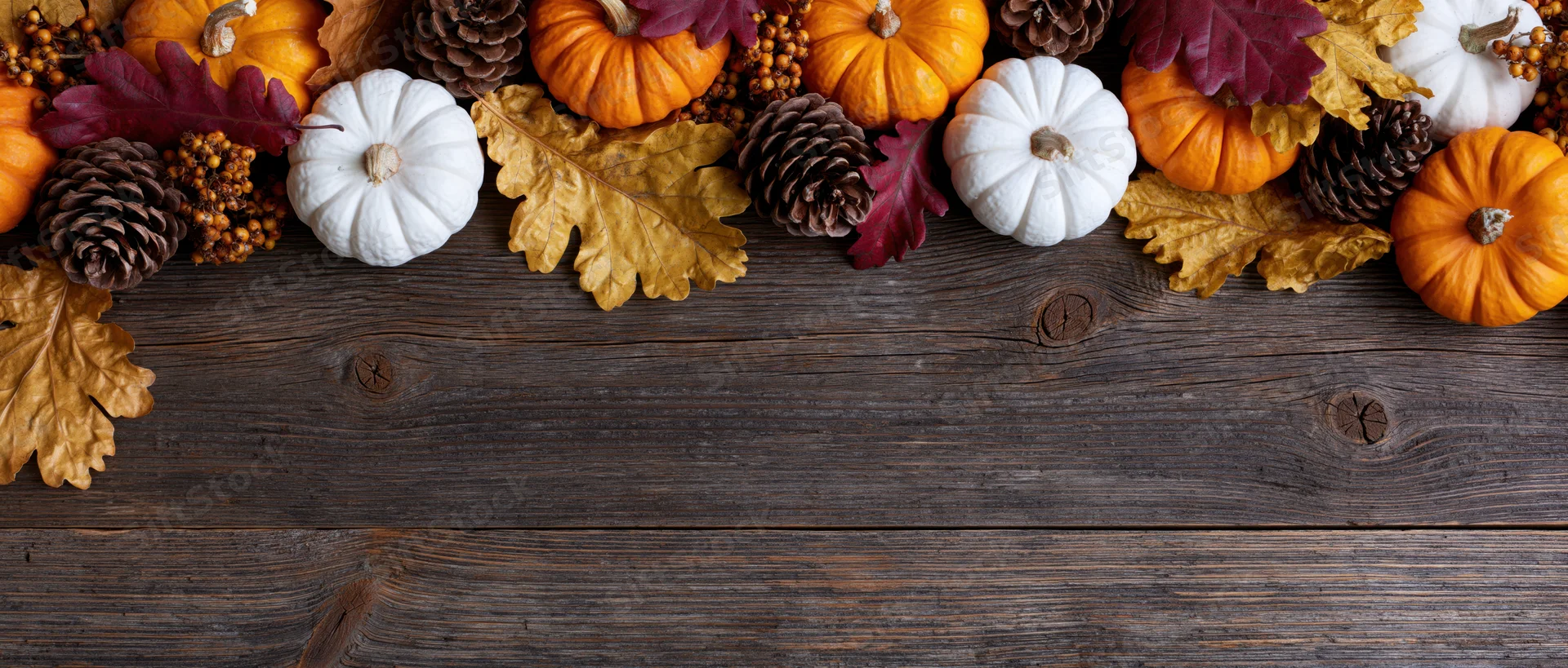 Small orange and white pumpkins arranged with autumn leaves and pinecones on a dark wooden table