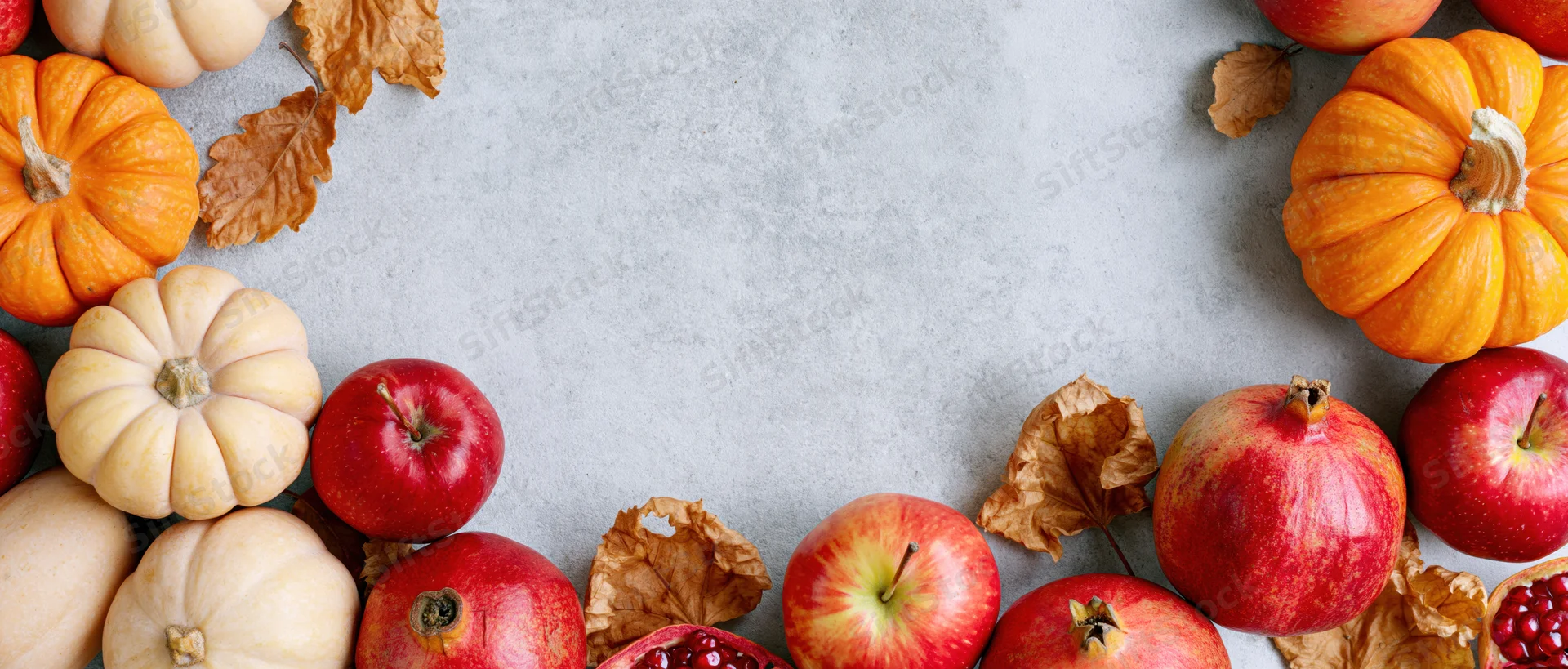 Autumn harvest flatlay arranged as a border frame with pumpkins apples pomegranates and leaves on gray surface