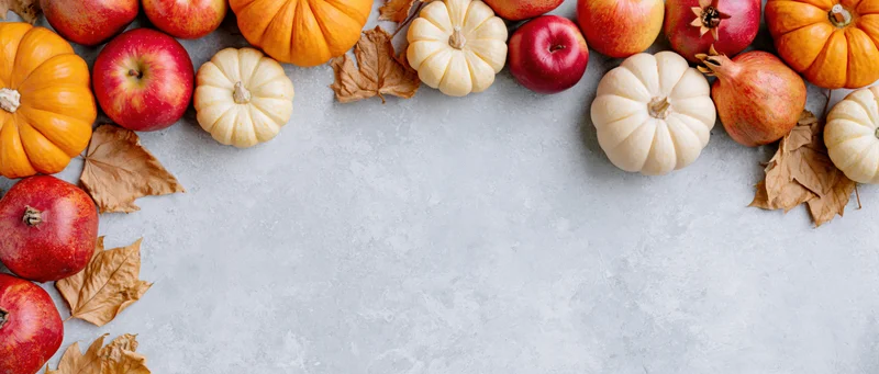 Autumn harvest flatlay arranged as a border frame with pumpkins, apples, and leaves on a concrete surface