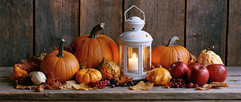 Autumn harvest still life with pumpkins, apples, and a lit lantern arranged on a rustic wooden table