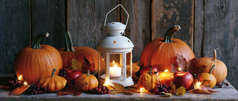 Pumpkins and apples arranged with a lit lantern and autumn leaves on a rustic wooden table
