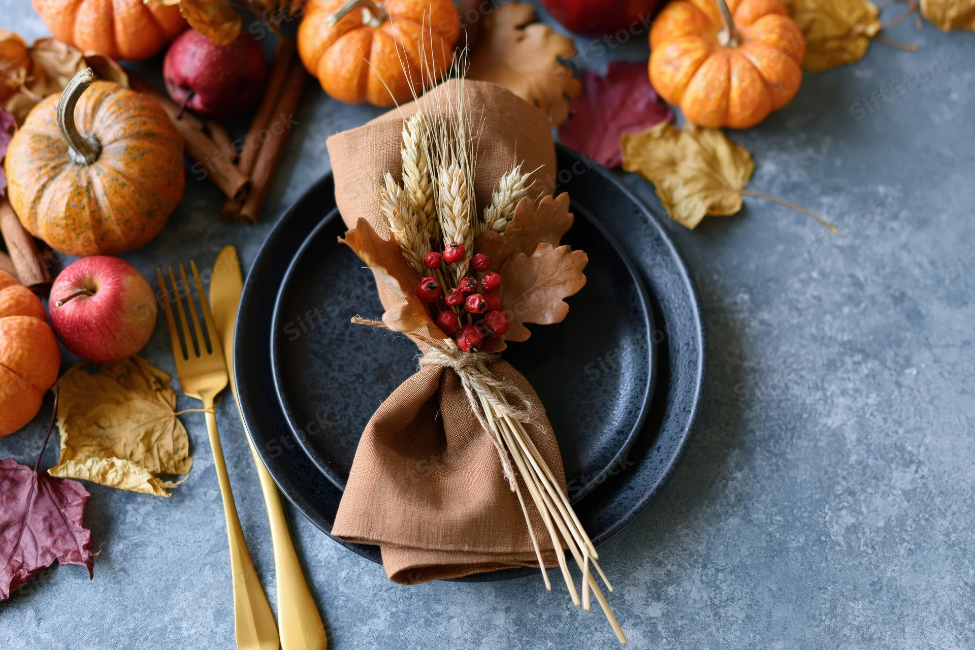 Overhead view of autumn harvest table setting with pumpkins, apples, wheat, and berries on dark plates and gray surface