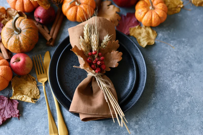 Overhead view of autumn harvest table setting with pumpkins, apples, wheat, and berries on dark plates and gray surface