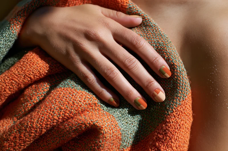 Woman's hand resting on a knitted scarf with orange and green nail art