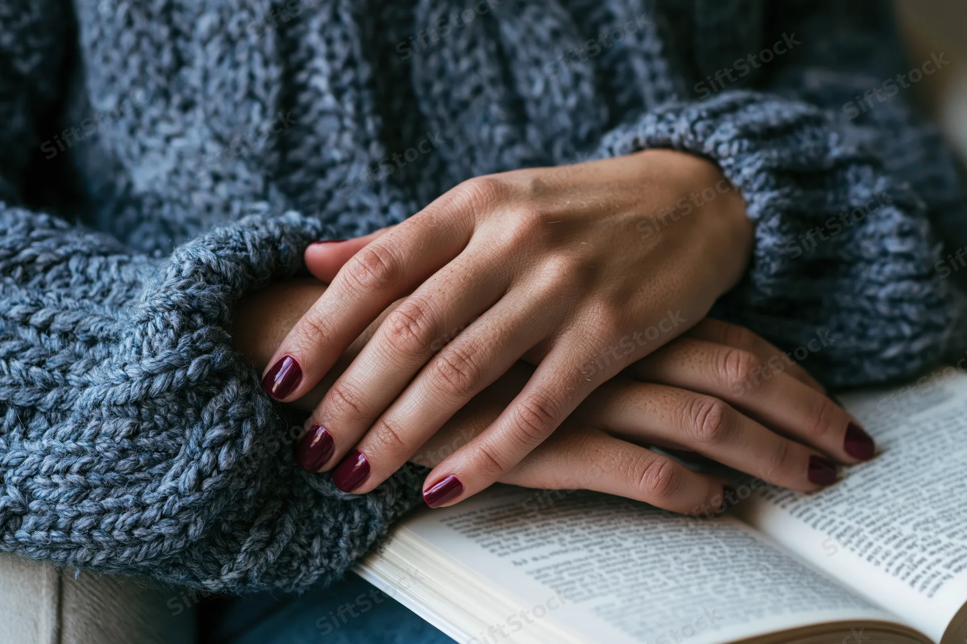 Woman's hands resting on an open book while wearing a gray knitted sweater