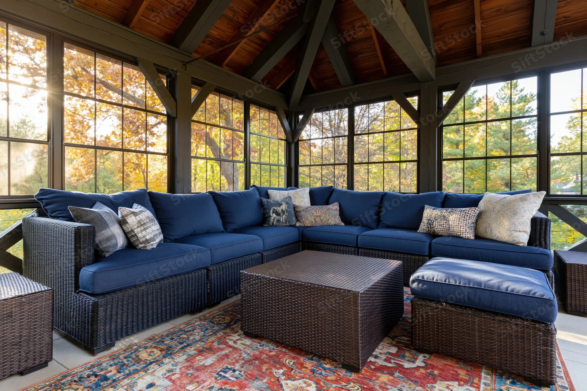 Blue wicker sectional sofa with patterned rug and large windows on a sunlit screened porch