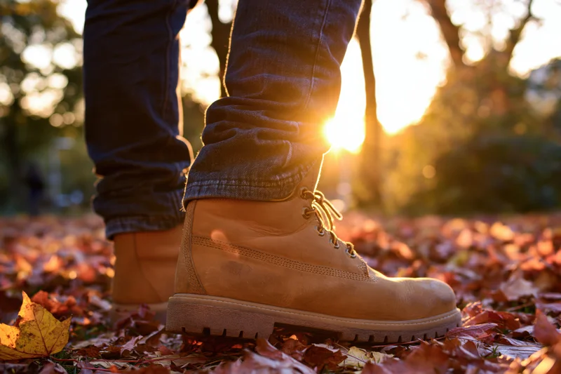 Low-angle view of boots on autumn leaves in a park at sunset