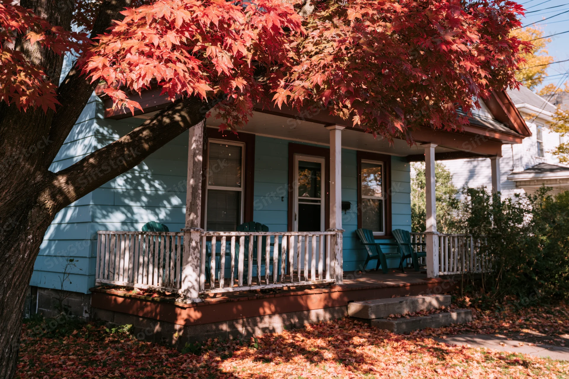Blue house with porch and red autumn leaves in front yard