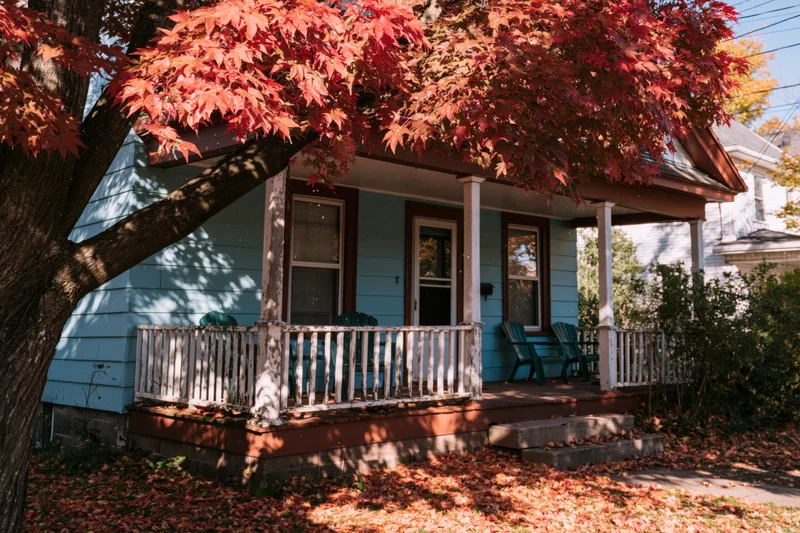 Blue house with porch and red autumn leaves in front yard