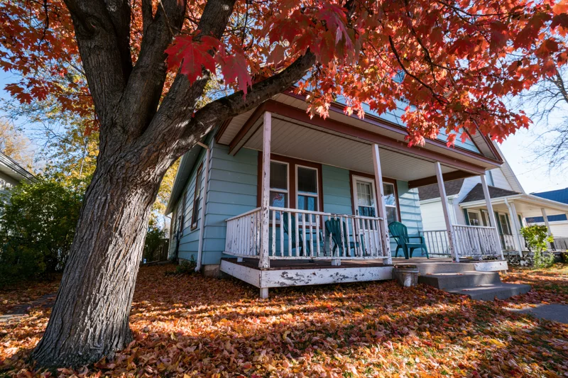 Blue house with porch and red maple tree in autumn front yard