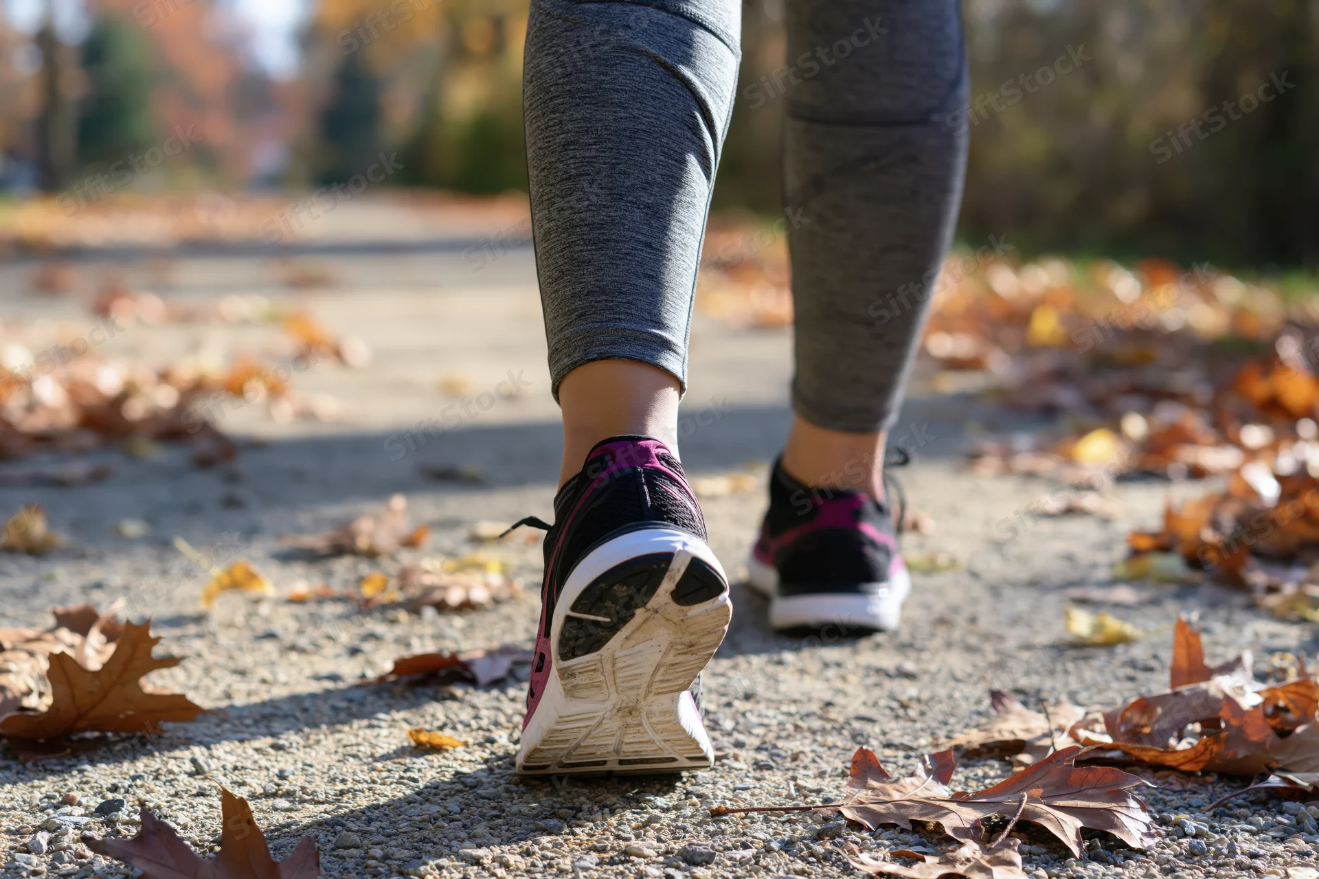 Woman running on a leaf-strewn pavement in autumn, wearing athletic sneakers and leggings