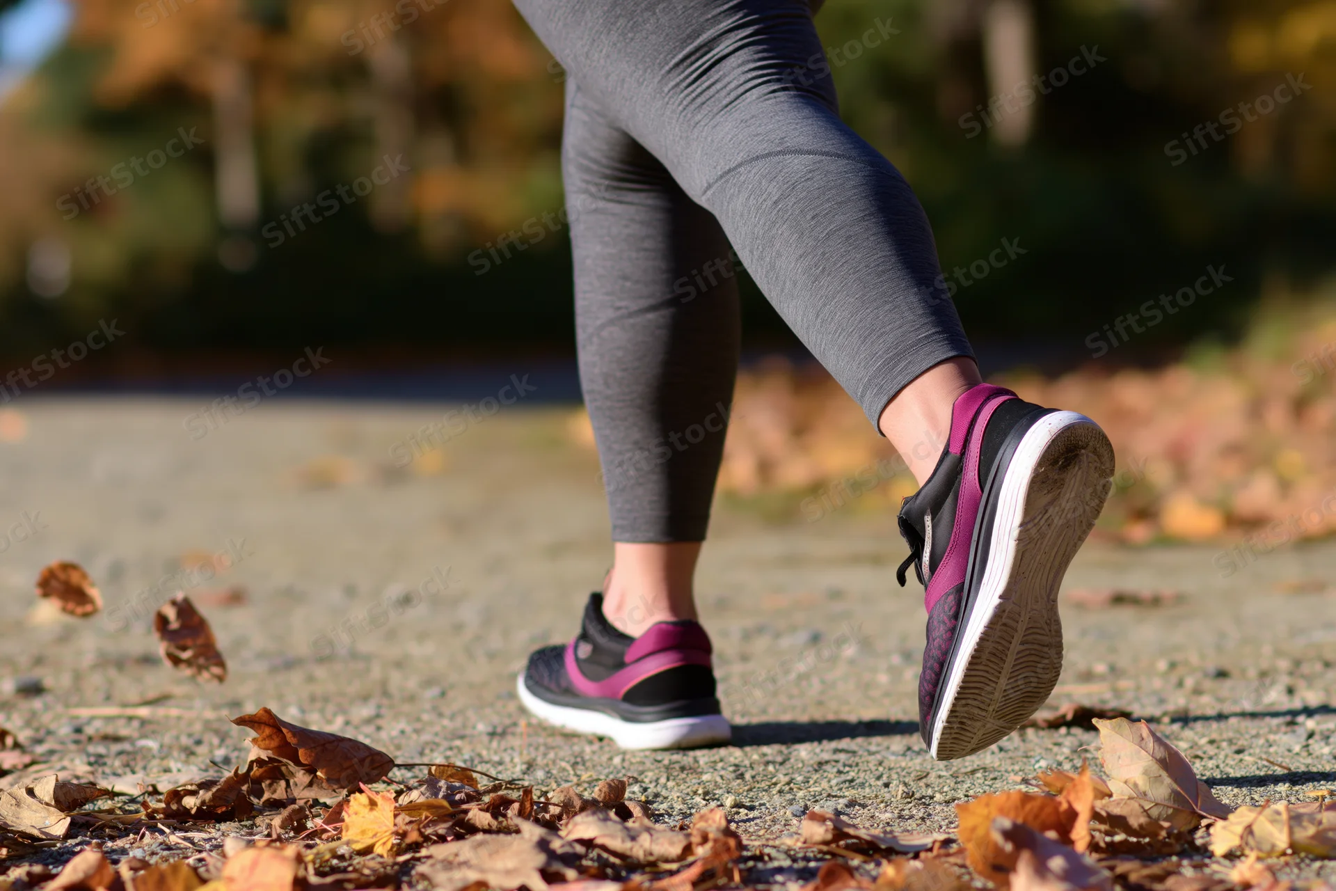Woman running on a leaf-strewn path in autumn, legs and sneakers in motion, outdoor fitness scene