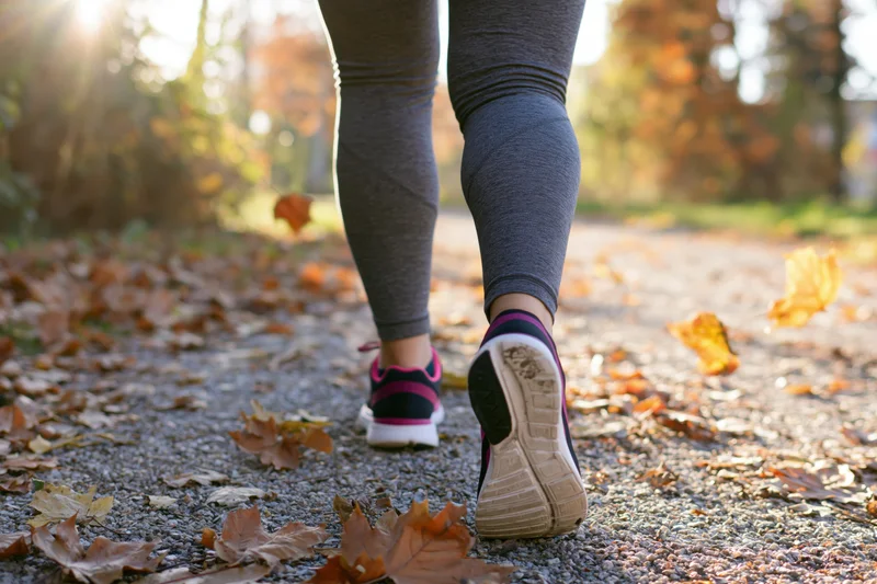 Woman running on a leaf-covered gravel path in autumn park