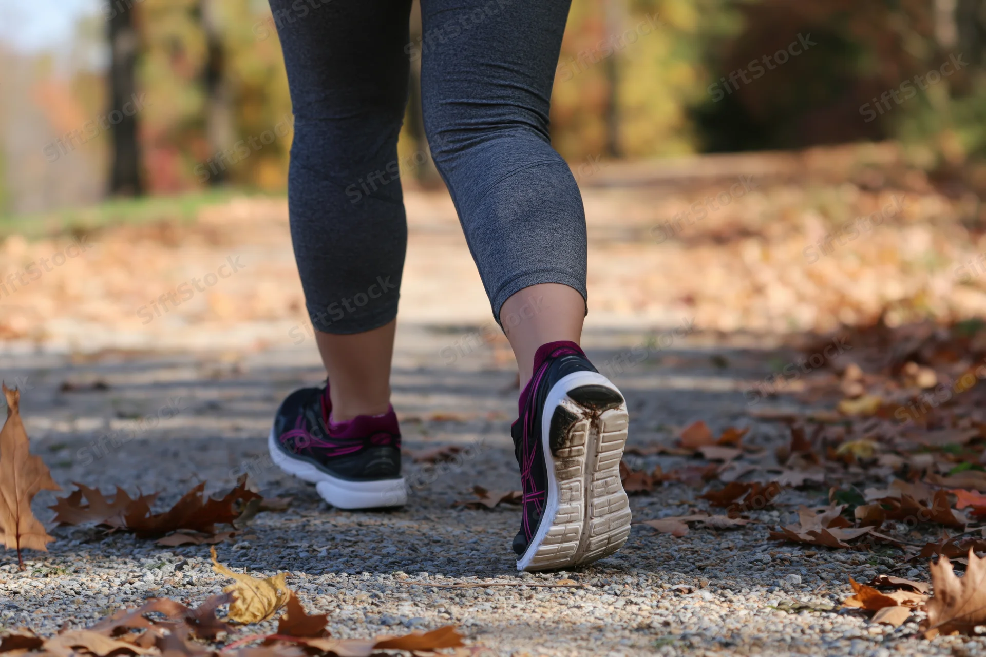 Woman running on a gravel path covered with autumn leaves in a park