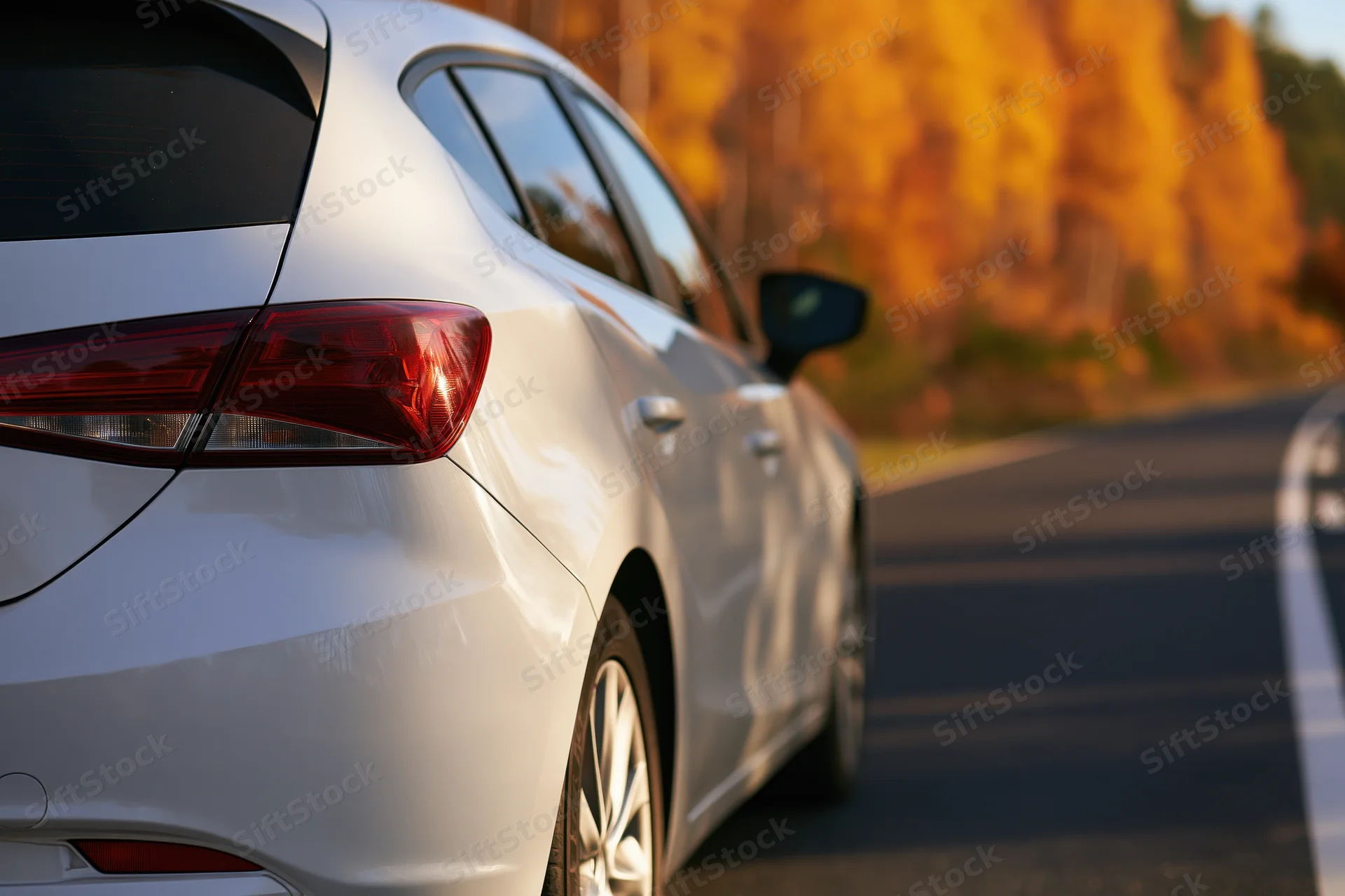 White hatchback driving on a road lined with golden autumn trees