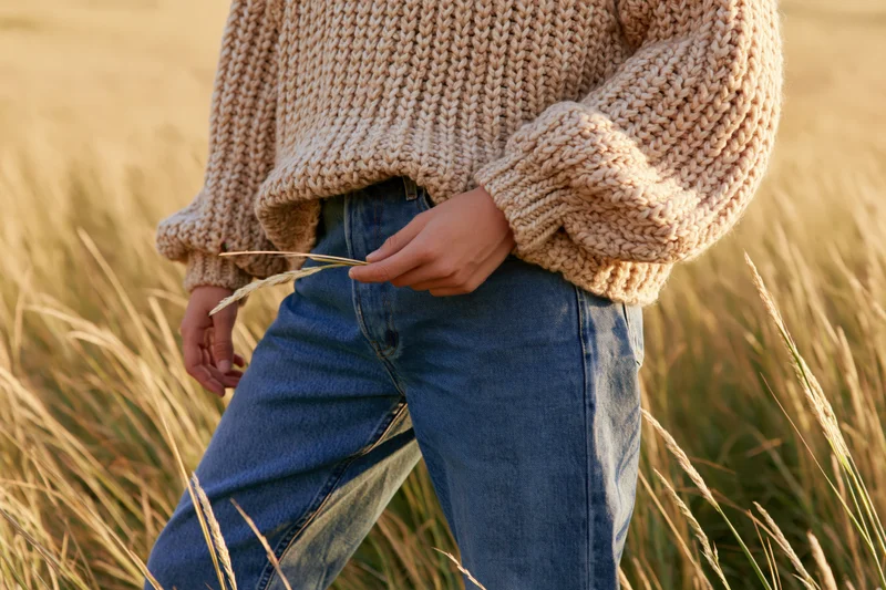 Woman in chunky beige knit sweater and jeans standing in a wheat field