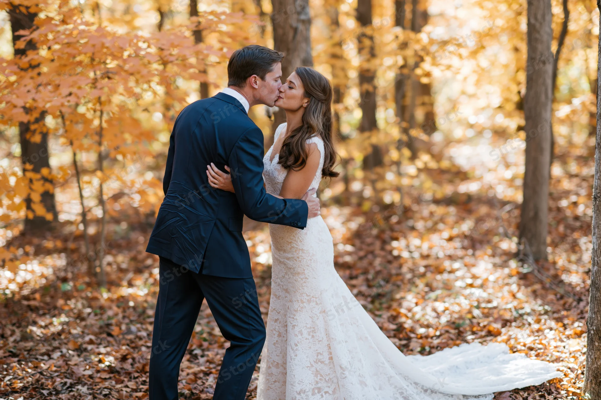 Bride and groom kissing in a sunlit autumn forest surrounded by golden leaves