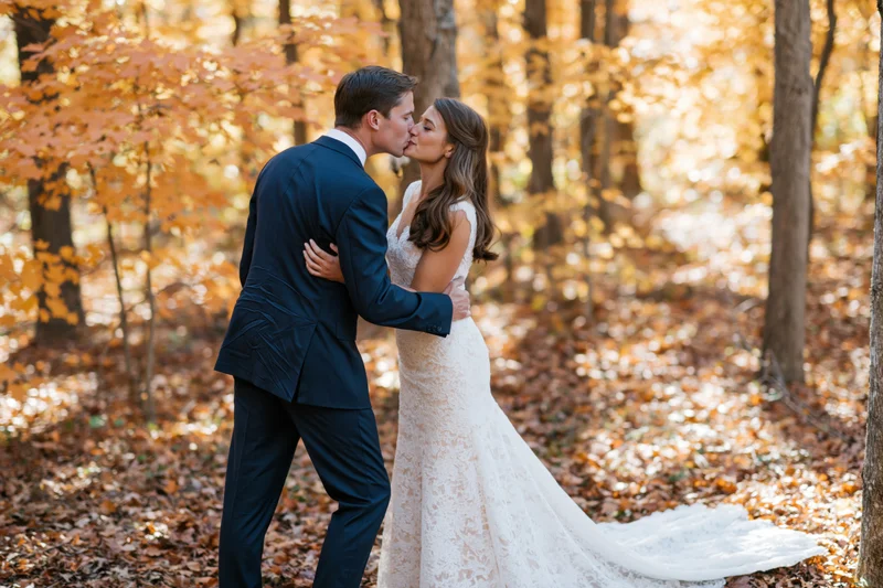 Bride and groom kissing in a sunlit autumn forest surrounded by golden leaves